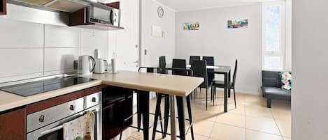 A modern kitchen with a dining area, featuring a built-in oven, a coffee maker, and a dining table with chairs.