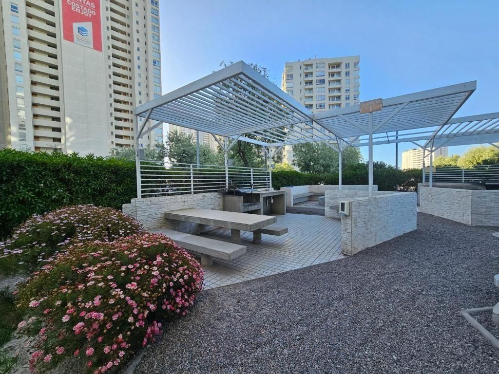 Un área de estar al aire libre con una pérgola, bancos y un jardín con flores rosas.