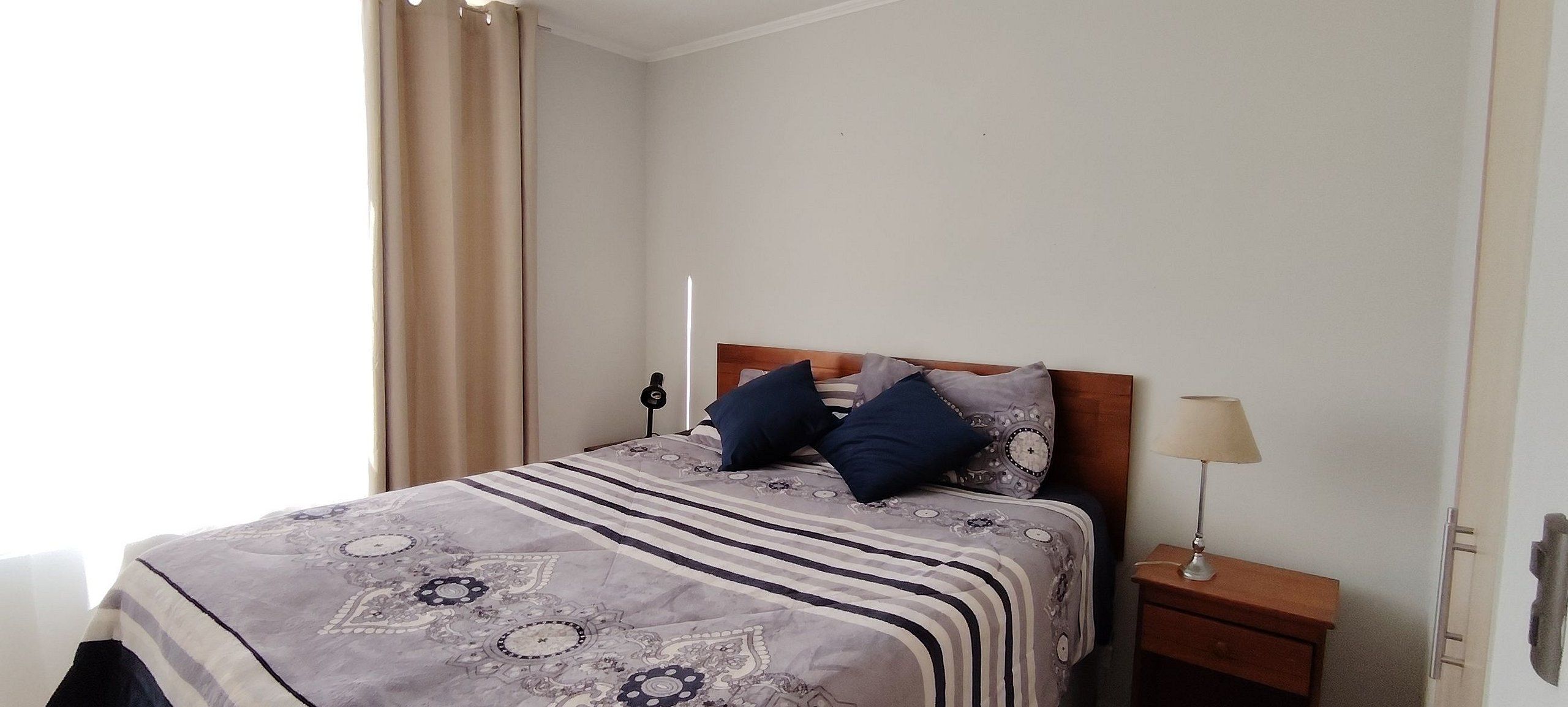 Una habitación de hotel con una cama, dos almohadas, una lámpara de noche y una mesita de noche.