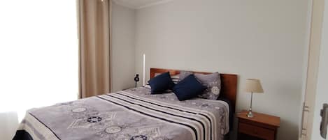 A hotel room with a bed, two pillows, a bedside lamp, and a nightstand.