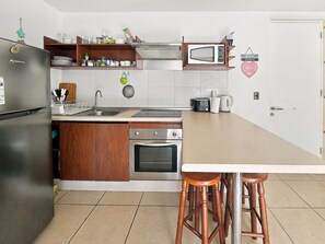 A kitchen with a refrigerator, stove, microwave, and bar stools.