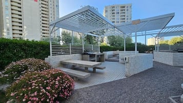 Ein Sitzbereich im Freien mit einer Pergola, Bänken und einem Garten mit rosa Blumen.