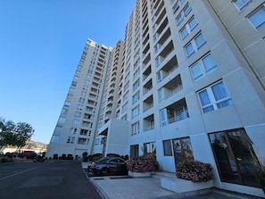 Un immeuble résidentiel à plusieurs étages, doté de balcons, d’un espace de stationnement et surplombant un ciel dégagé.