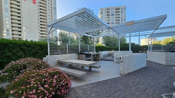 Un espace extérieur aménagé avec une pergola, des bancs et un jardin où poussent des fleurs roses.