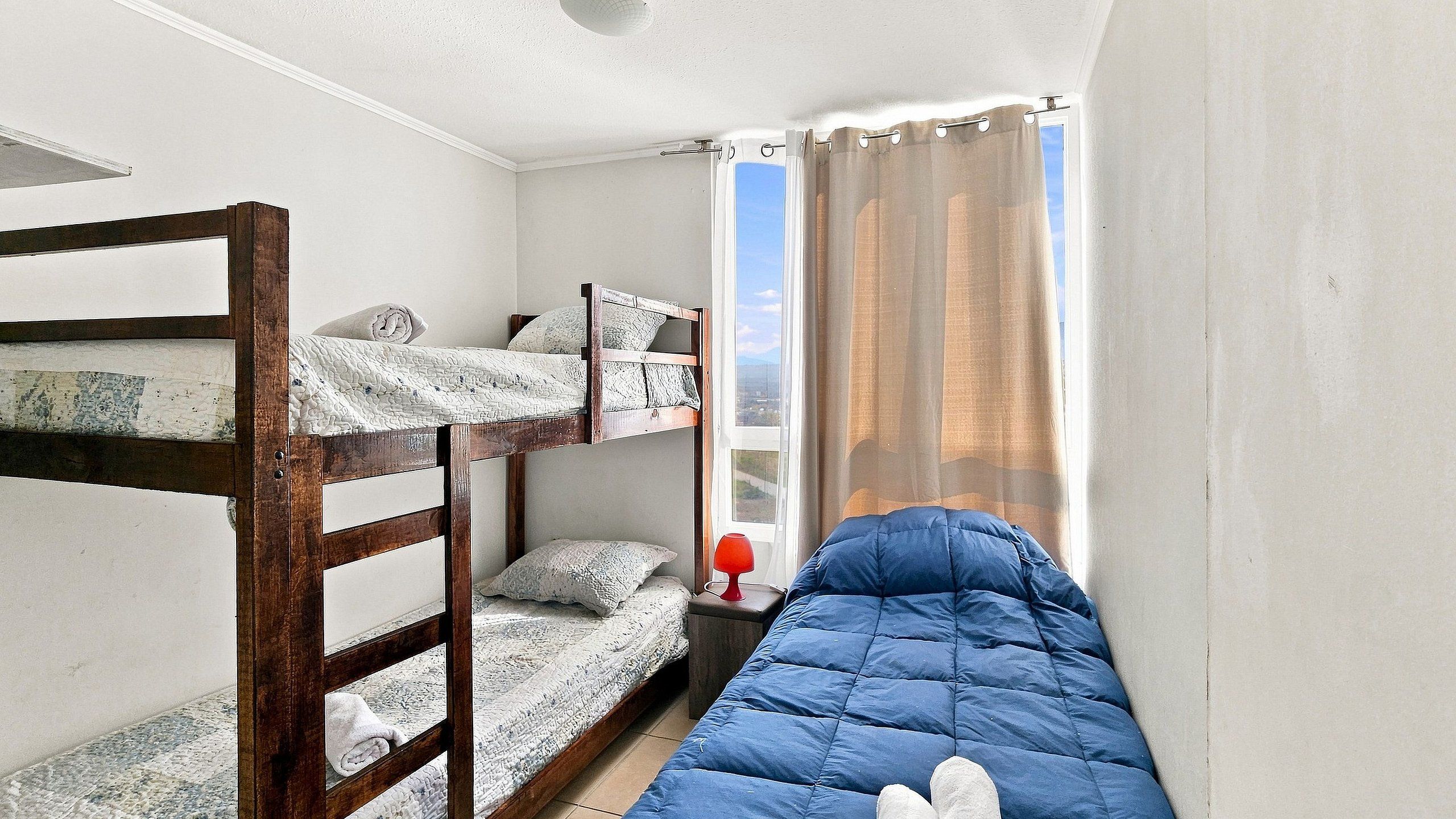 A dormitory room with bunk beds, a window with curtains, and a red lamp on a bedside table.