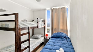 Un dormitorio con literas, una ventana con cortinas y una lámpara roja sobre una mesita de noche.