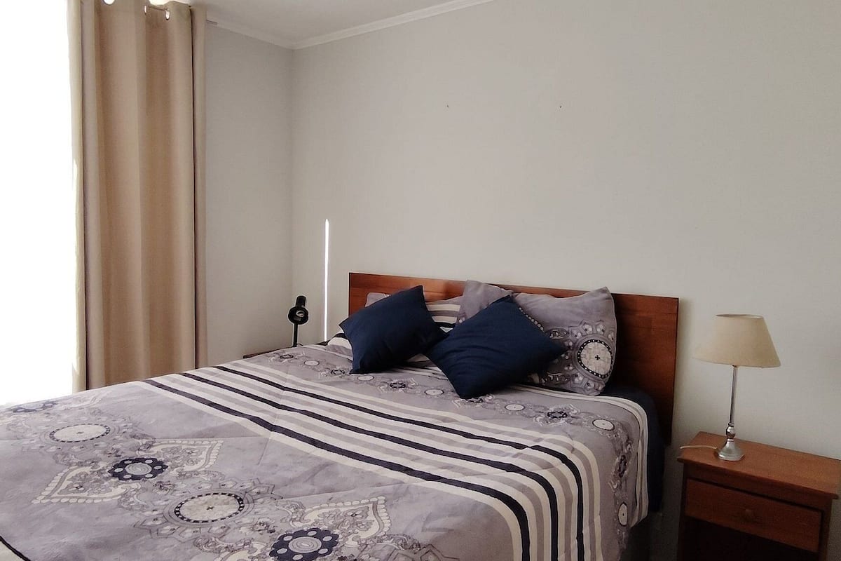 Quarto de hotel com cama, duas almofadas, abajur e mesa de cabeceira.