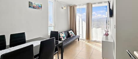 A modern living room with a dining area, large windows, and a view of the cityscape.