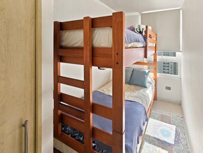 Cama individual con estructura de madera, colchón y almohadas. Debajo de la cama hay un pequeño estante con zapatos.