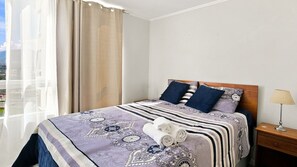 A hotel room with a bed, a nightstand, a lamp, and a window with curtains. - Oceana Suites Marina del Sol (Coquimbo)