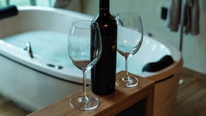 Un plan de travail en bois avec une bouteille de vin et deux verres, une baignoire et un peignoir accroché au mur.