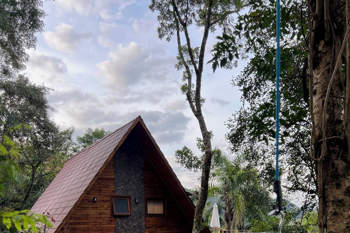 A wooden cabin with a sloped roof, surrounded by trees and a grassy area.