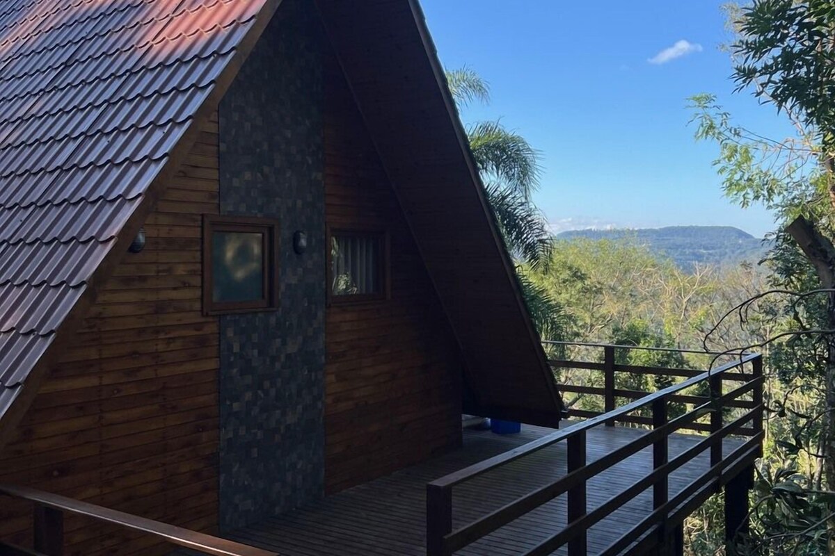 A wooden cabin with a sloped roof, a balcony, and a view of the surrounding forest.