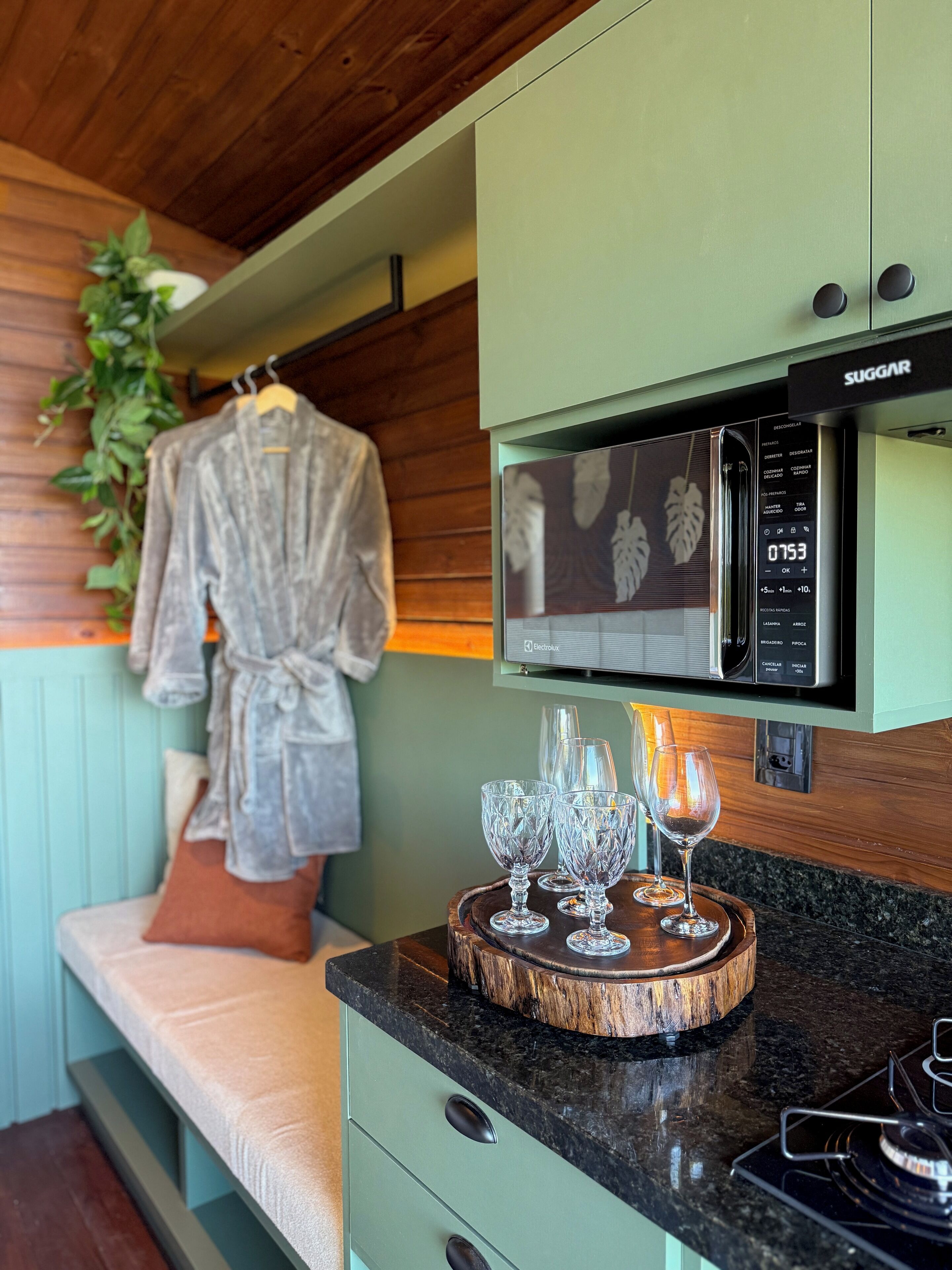 A kitchenette with a microwave, a wooden tray with glasses, and a bench with a robe hanging.