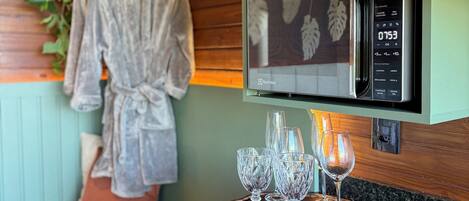 A kitchenette with a microwave, a wooden tray with glasses, and a bench with a robe hanging.