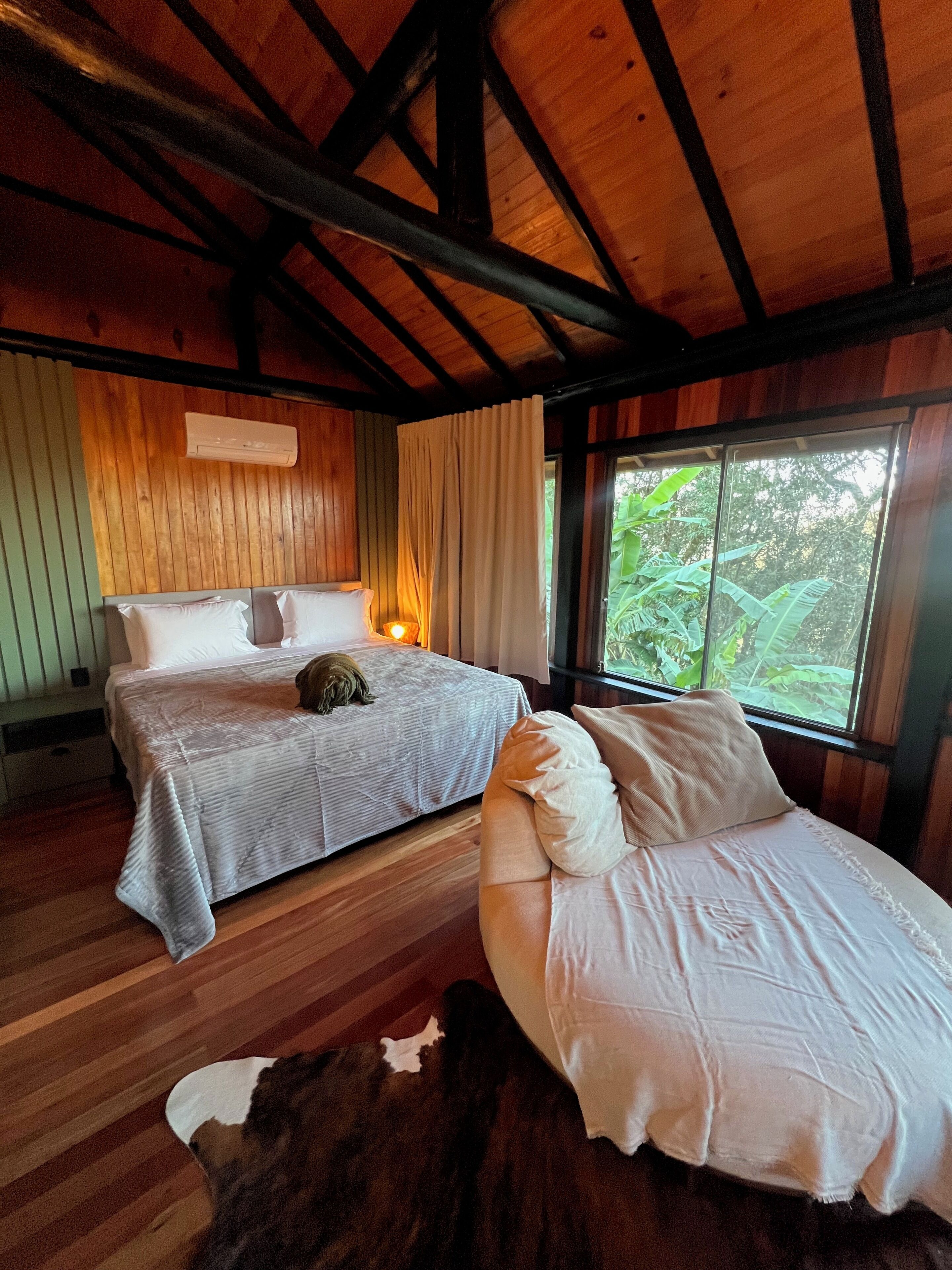 Une chambre de style cabane en bois, avec deux lits, une fenêtre donnant sur un paysage verdoyant et un plafond avec des poutres apparentes.