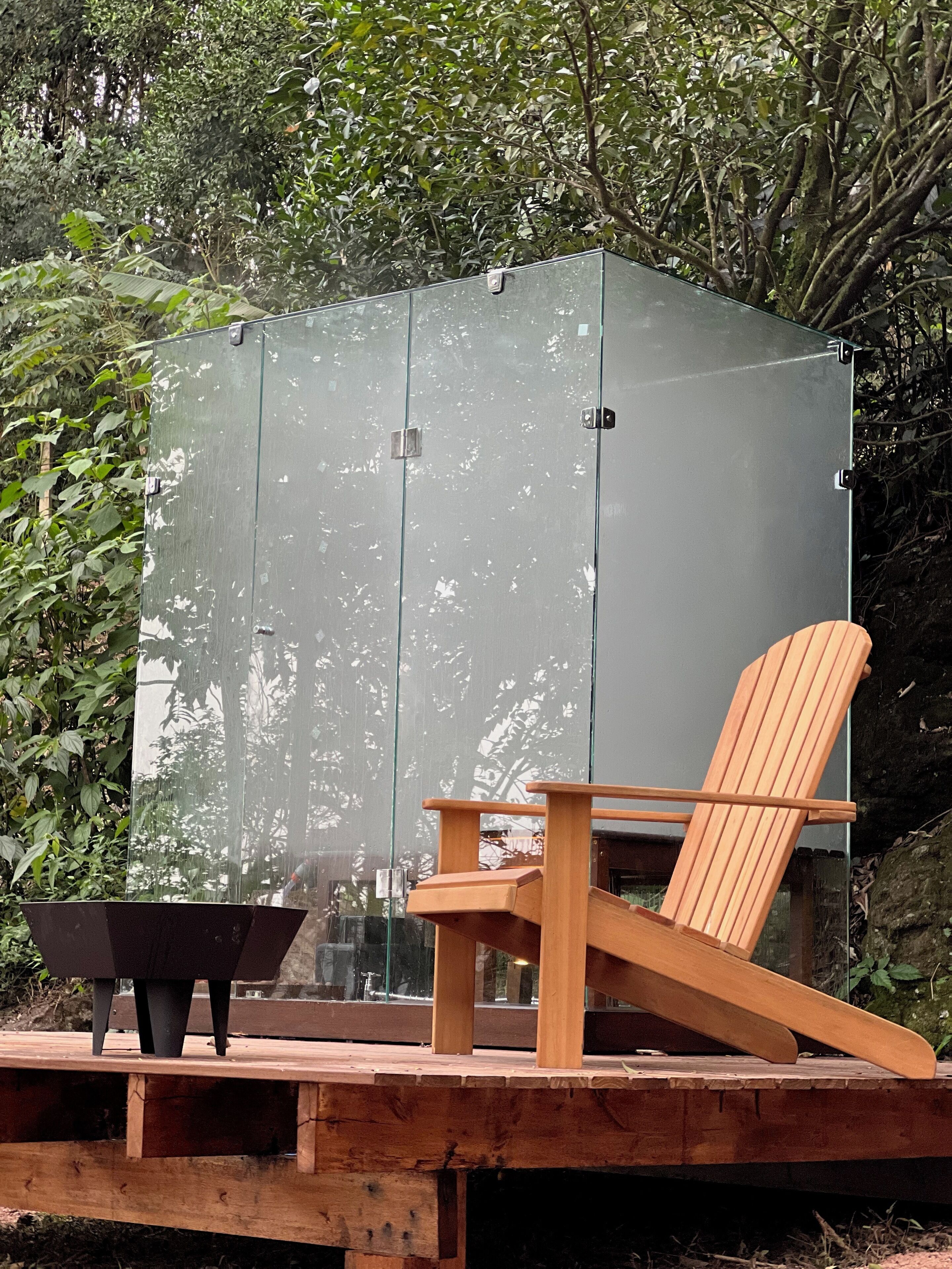 Una terraza de madera con cerramiento de vidrio, una silla de madera y una maceta negra.