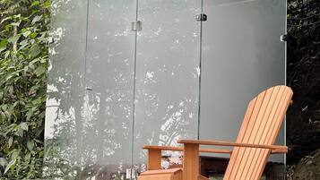 Una terraza de madera con cerramiento de vidrio, una silla de madera y una maceta negra.