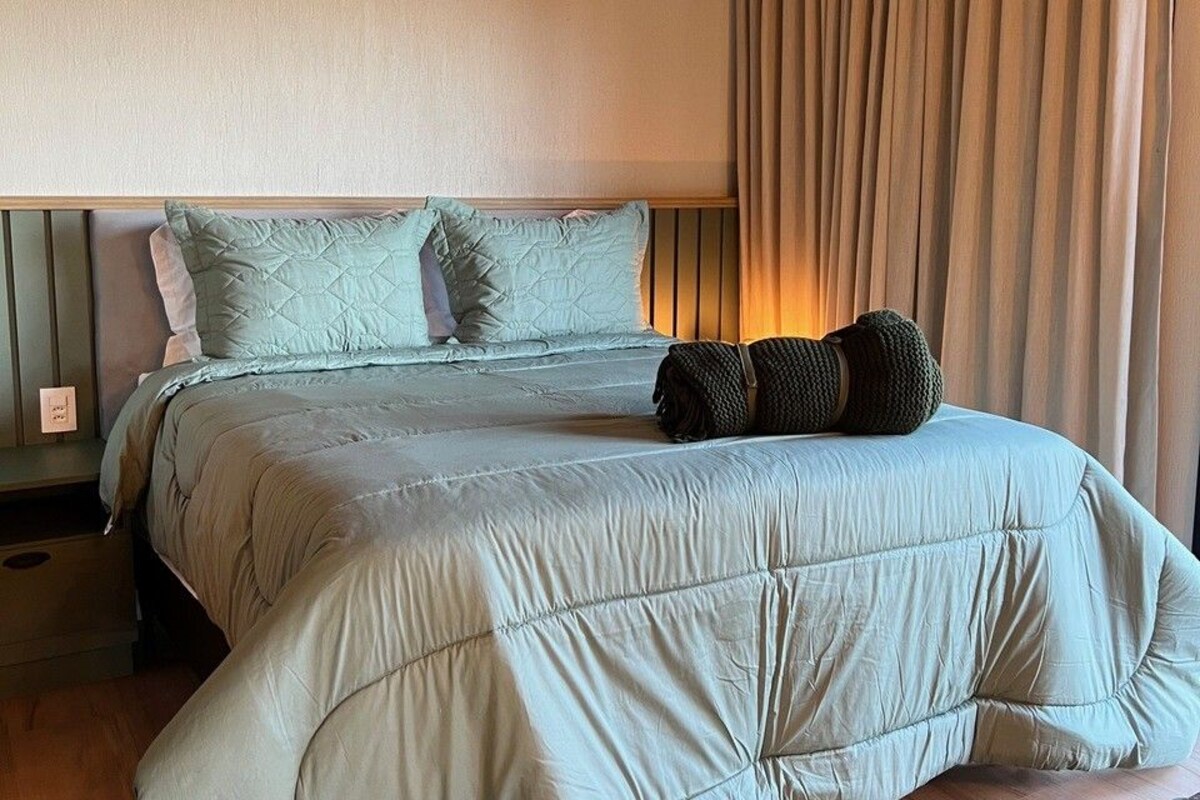 A neatly made bed with a quilted headboard, a bedside lamp, and a window with curtains.