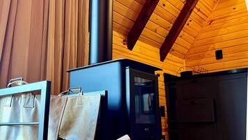 Interior acogedor de una cabaña con estufa de leña, un sofá y un bolso, y techo de madera.