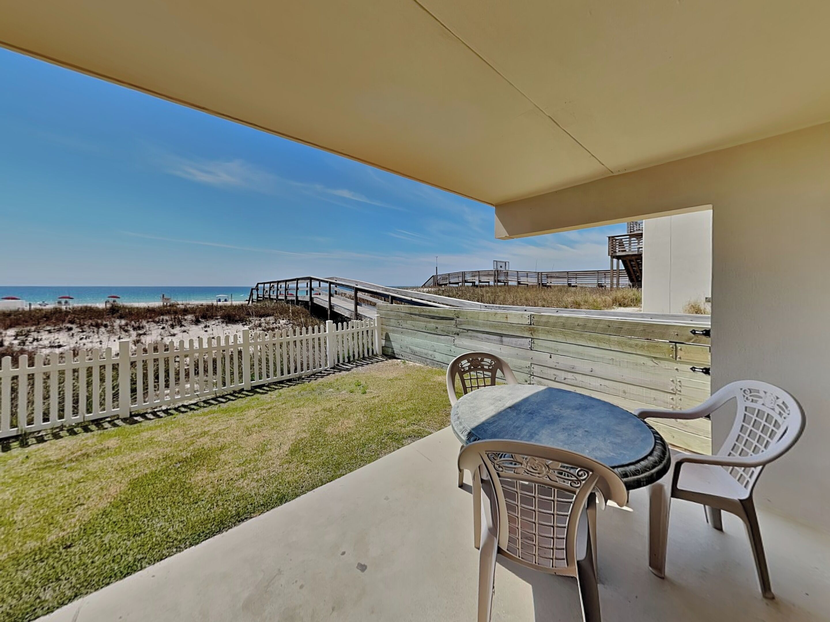 A balcony with a view of the beach, a wooden fence, and a table with chairs.
