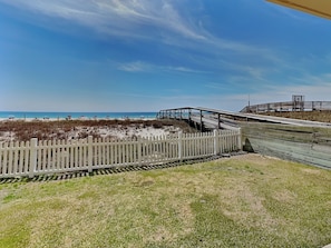 A beach with a wooden boardwalk, a white picket fence, and a clear blue sky.