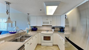 A modern kitchen with white cabinets, stainless steel appliances, a built-in microwave, and a large refrigerator. - Ocean Breeze West #106 | Gulf-Front, Ground Floor, Pool, Beach Access (Perdido Key)