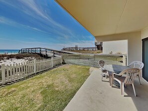 Un balcon donnant sur la plage, une clôture blanche en bois et une table avec des chaises.