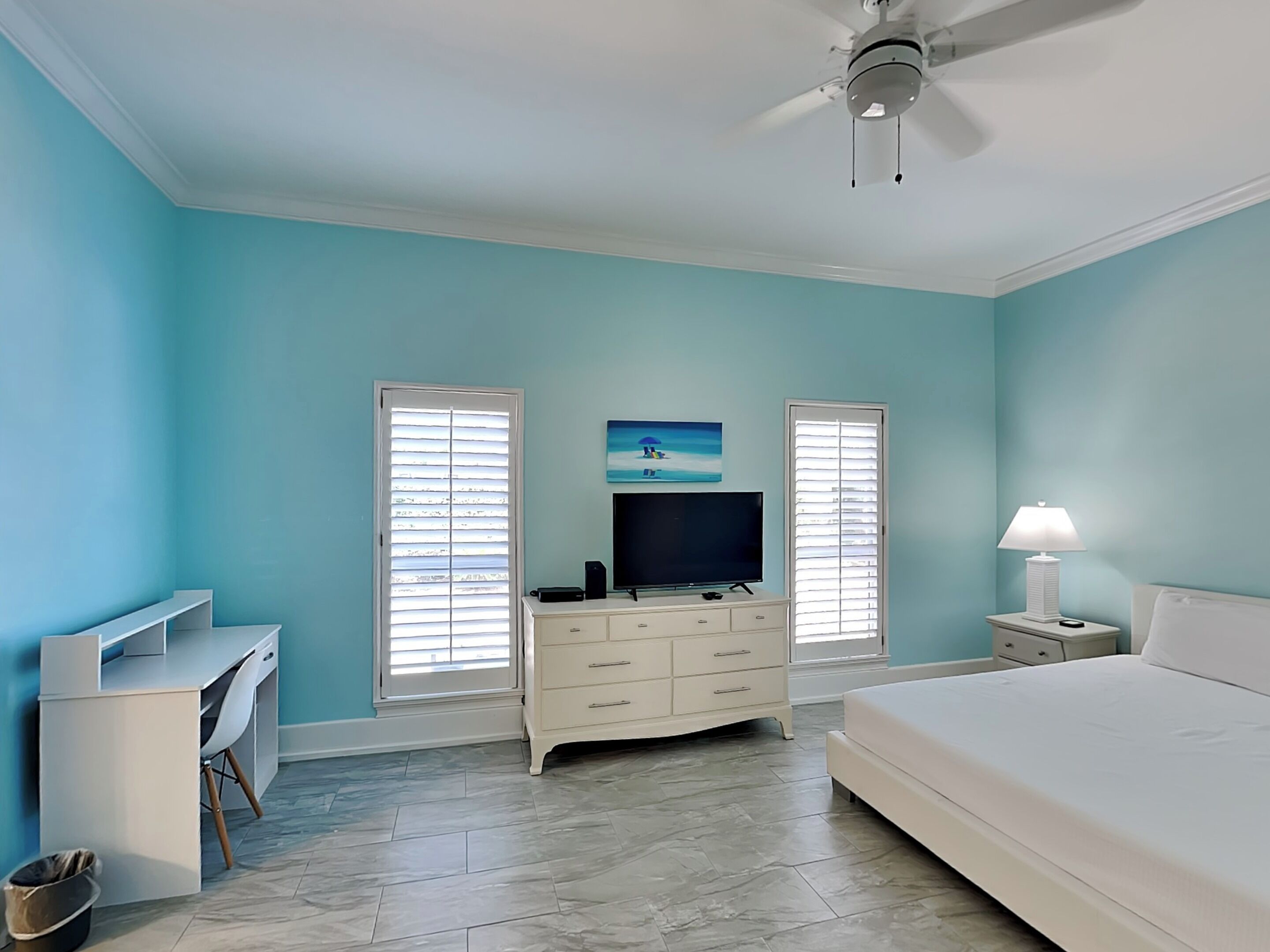 A bedroom with a bed, a desk, a dresser, a television, and a ceiling fan.