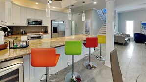 Una cocina moderna con armarios blancos, electrodomésticos de acero inoxidable y una isla central con taburetes de colores.