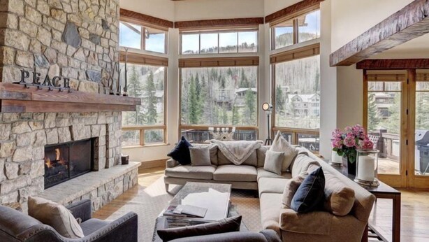 Una sala de estar acogedora con chimenea de piedra, ventanas amplias y vistas al bosque circundante.