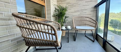 A balcony with wicker chairs, a small table, and a potted plant.