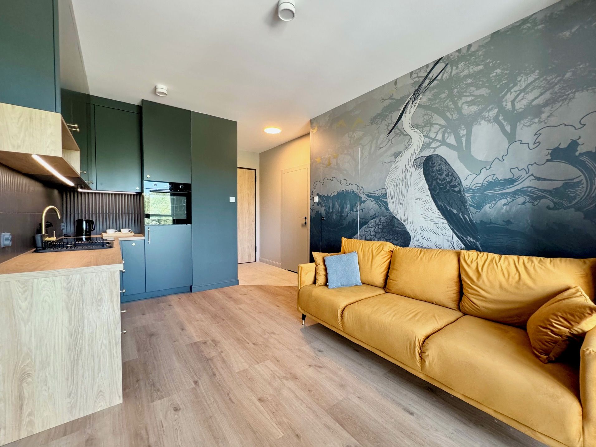 A modern living space with a kitchen, a sofa, and a large wall mural.