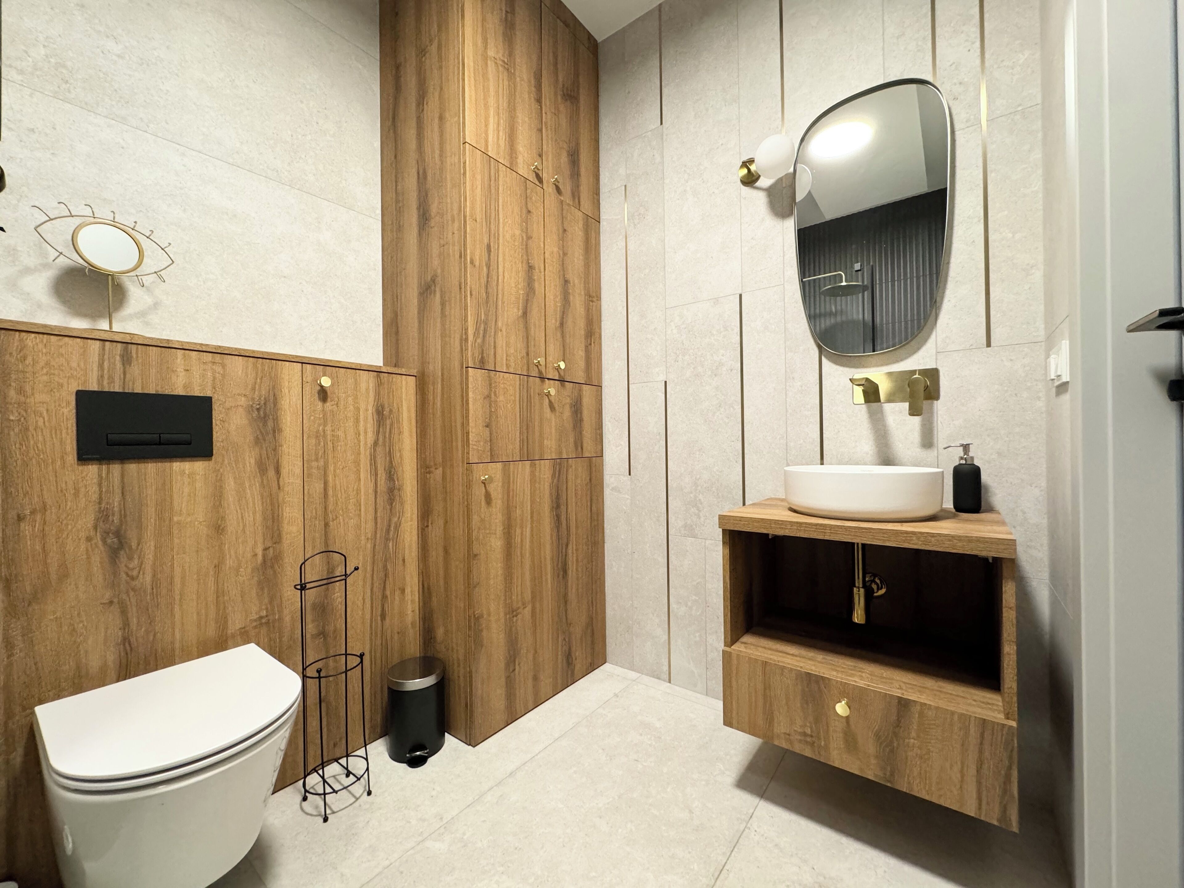 A modern bathroom with a wooden vanity, a round mirror, and a toilet.