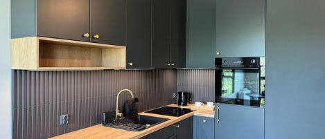 A modern kitchen with dark cabinetry, a wooden countertop, a built-in stove, and a coffee maker.