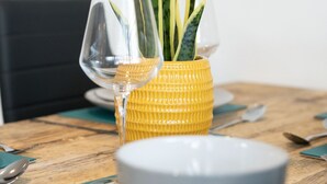 Ein Esstisch mit einer gelben, strukturierten Vase, darin eine Pflanze, eine weiße Schüssel und ein Weinglas.