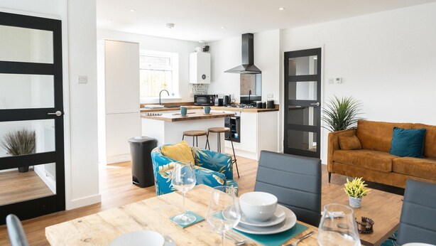 Eine moderne Küche mit Kochinsel, ein Essbereich mit Holztisch und ein Wohnzimmer mit Sofa und Couchtisch.