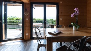 Un interior de madera con una mesa de comedor, sillas y vistas a una terraza exterior a través de amplios ventanales.