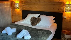 Un dormitorio de cabaña de madera con cama, almohadas, un cojín con forma de corazón y una colcha.