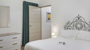 A bedroom with a bed, a dresser, a door, and a wall-mounted lamp. - Casa Alma by Wonderful Italy (Genoa)