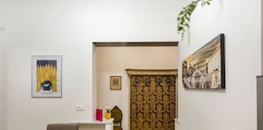 A room with a white wall, a framed picture of a forest, a framed picture of a building, a plant hanging from the ceiling, and a chair with a cushion. - Casa Alma by Wonderful Italy (Genoa)