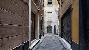 A narrow alleyway with closed shop fronts and a building with a small window and door. - Casa Alma by Wonderful Italy (Genoa)