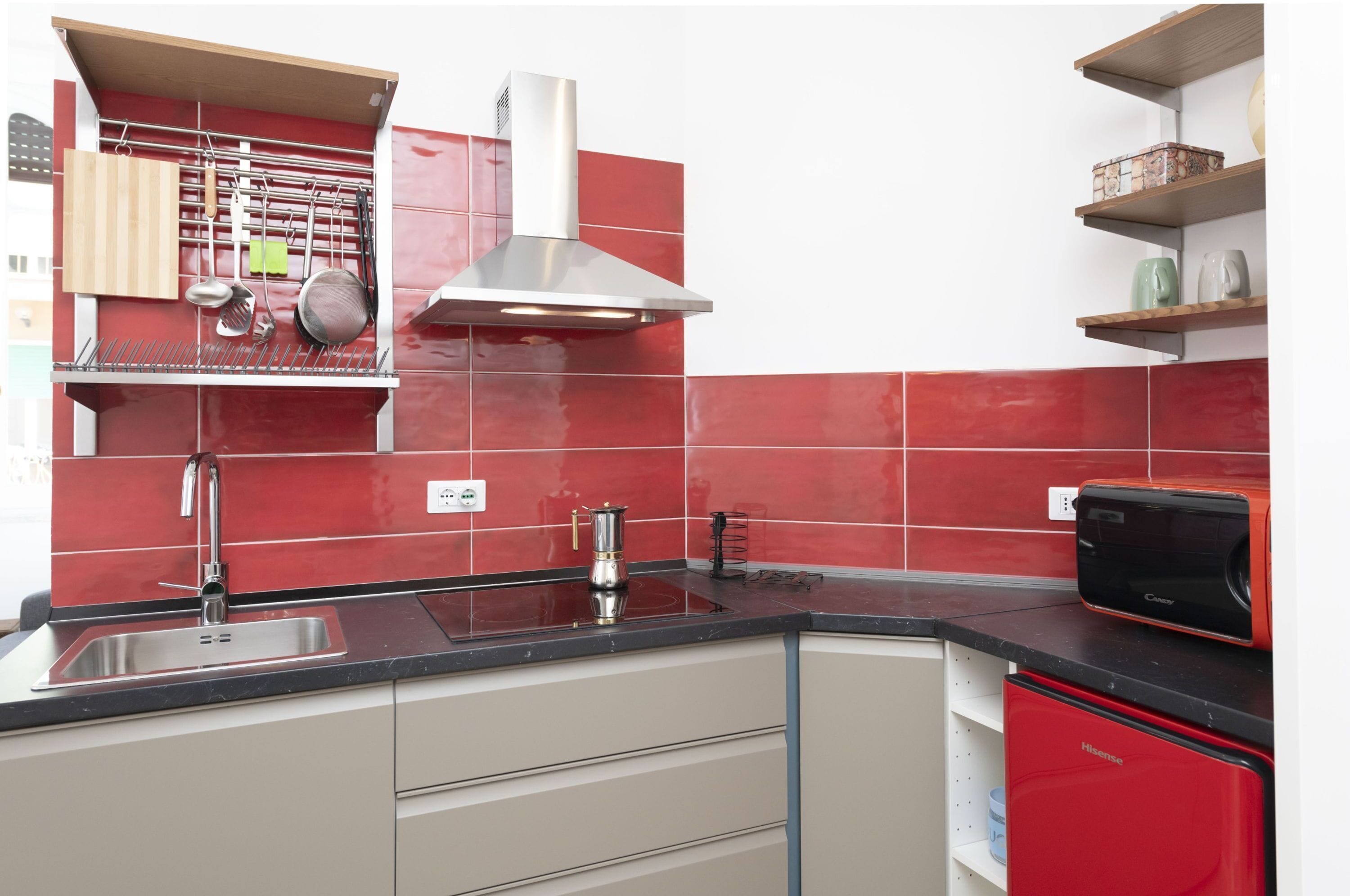 Una cucina con piastrelle rosse, un lavello in acciaio inossidabile, una lavastoviglie rossa e un forno a microonde.