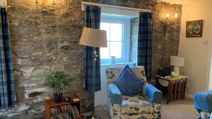 A cozy room with a stone wall, a blue plaid chair, a bookshelf, and a lamp. - 1 bedroom cottage in Blair Atholl Pitlochry.     New listing.  (Blair Atholl, Pitlochry,)