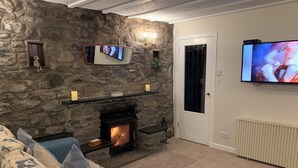 A cozy living room with a stone fireplace, a sofa with floral cushions, a flat-screen TV mounted on the wall, and a door leading to another room. - 1 bedroom cottage in Blair Atholl Pitlochry.     New listing.  (Blair Atholl, Pitlochry,)