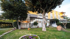 A landscaped garden with a flower bed, a tree, and a building in the background. - HOTEL HRS (Follonica)