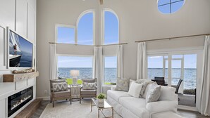 Un salon spacieux doté d’une cheminée, d’un canapé blanc, d’une table basse et offrant une vue sur la mer grâce à de grandes fenêtres.