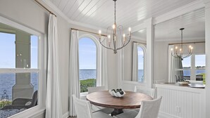 Un coin repas avec une table ronde en bois, des chaises en osier blanc et un lustre.