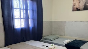 A hotel room with two beds, a window with blue curtains, a painting on the wall, and a striped rug on the floor.