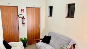 A room with two wooden doors, a fire extinguisher, a grey sofa, a wooden bench, and a small window.
